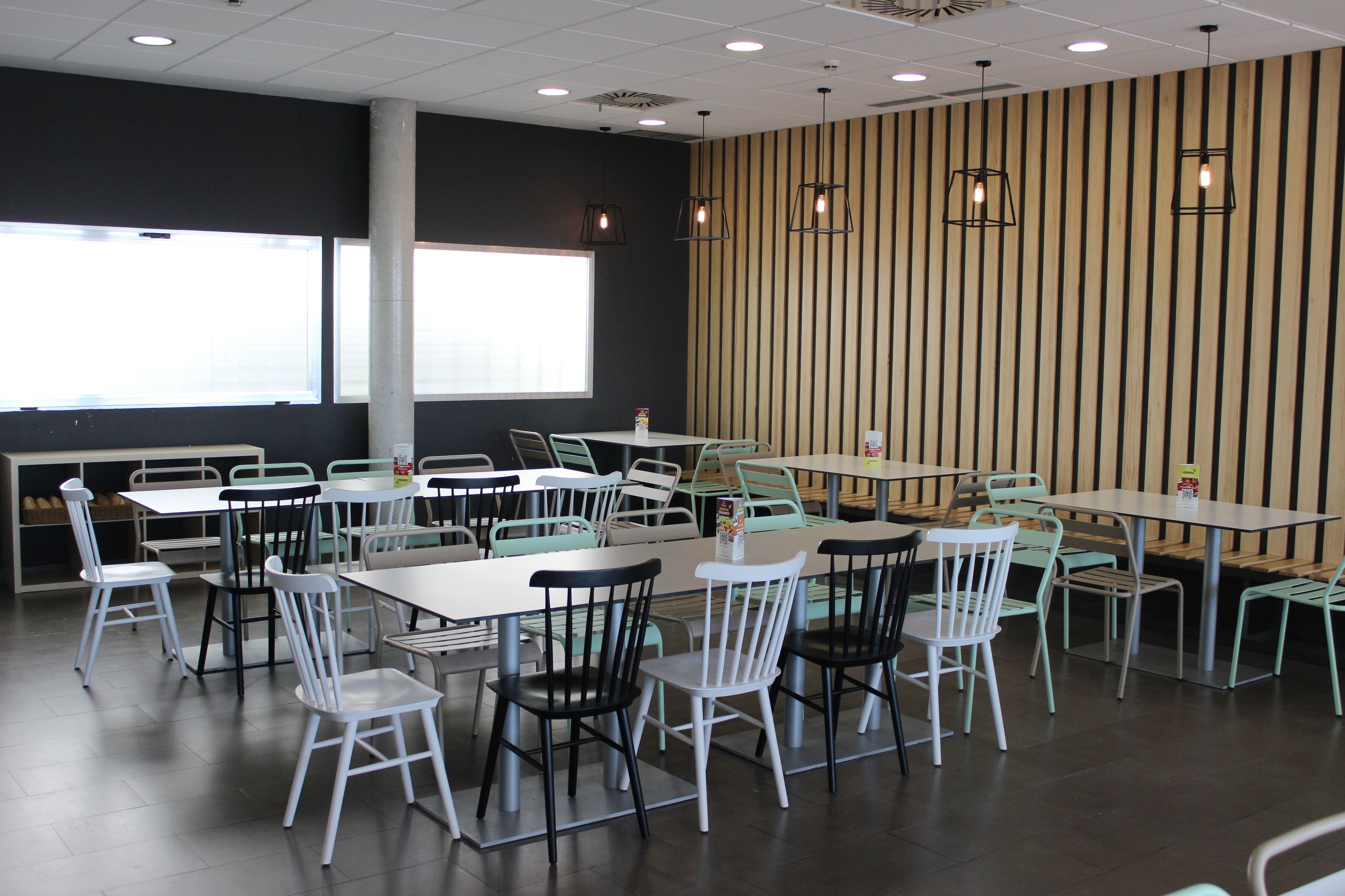 A dining area with multiple tables and chairs, large windows, and a striped wall.