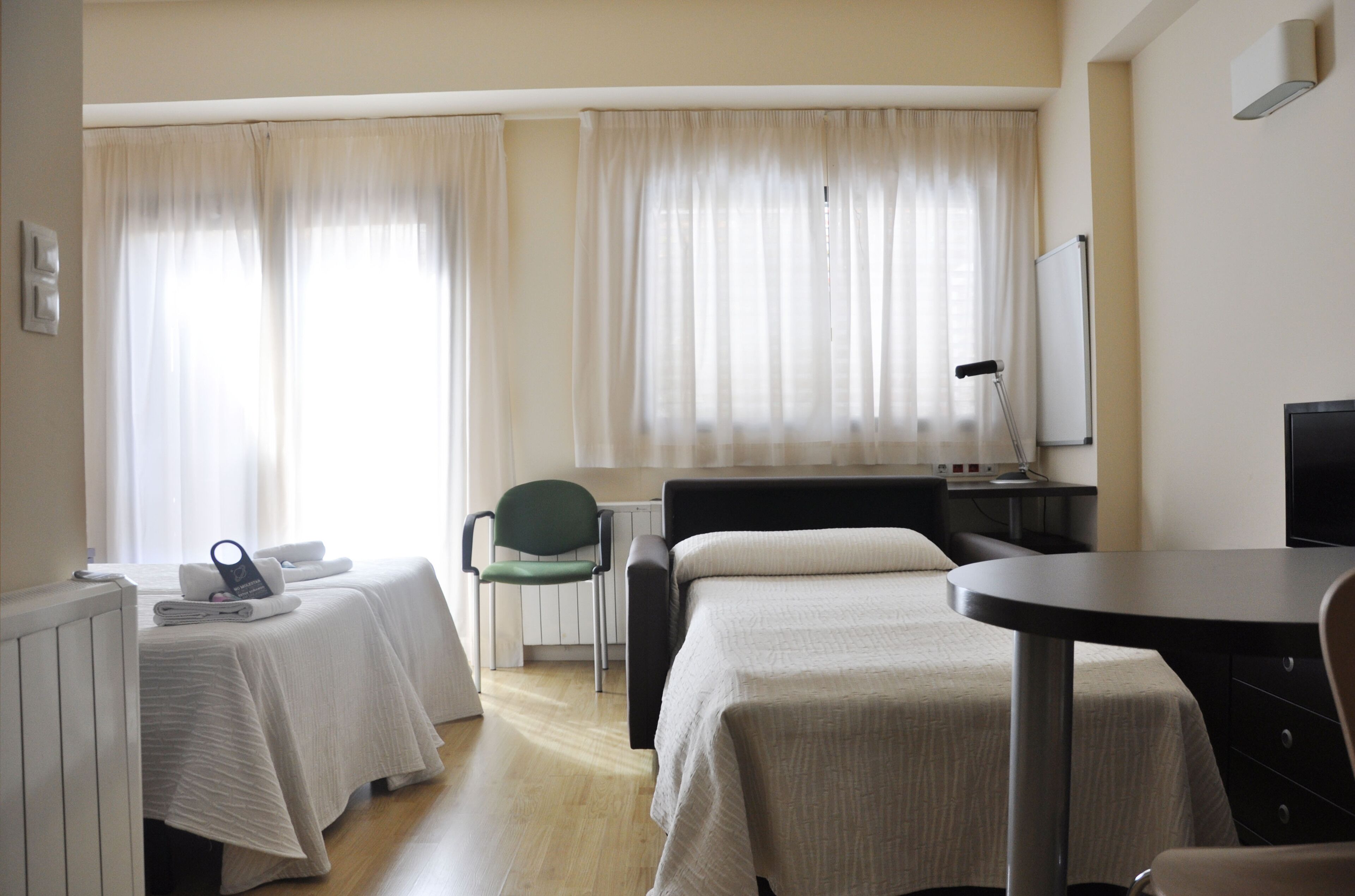 Habitació d'hotel amb dos llits, una taula de treball, una cadira, un radiador i una televisió.