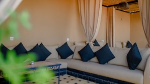 A beige sofa with black cushions, a patterned table, and a checkered floor.