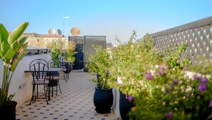 A rooftop patio with outdoor seating, potted plants, and a view of the city skyline.