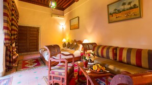 A cozy room with a wooden ceiling, a bed with pillows, a sofa, a table with fruit, and a painting on the wall.