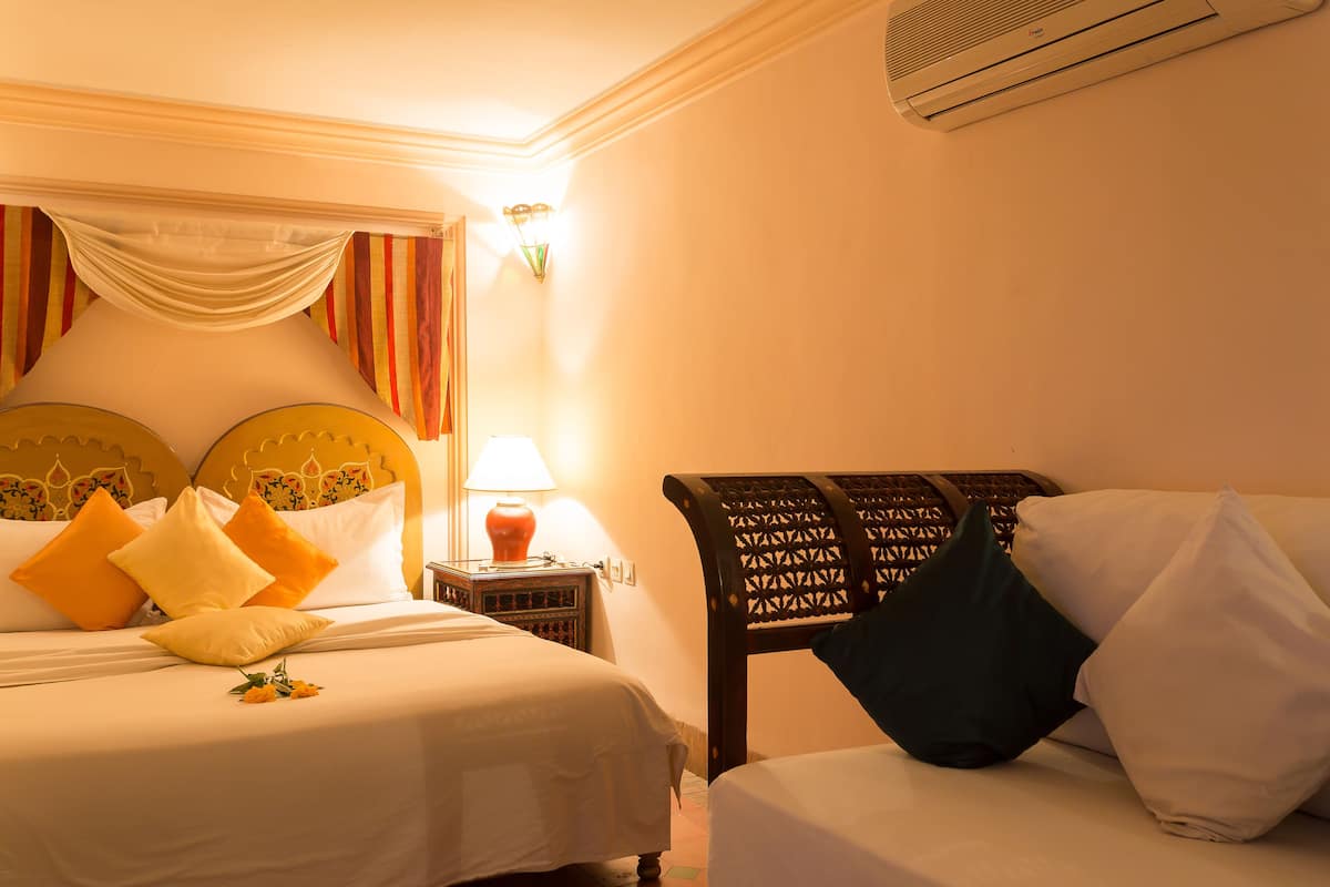 Una camera d'albergo con due letti, un comodino, una lampada e un condizionatore d'aria.