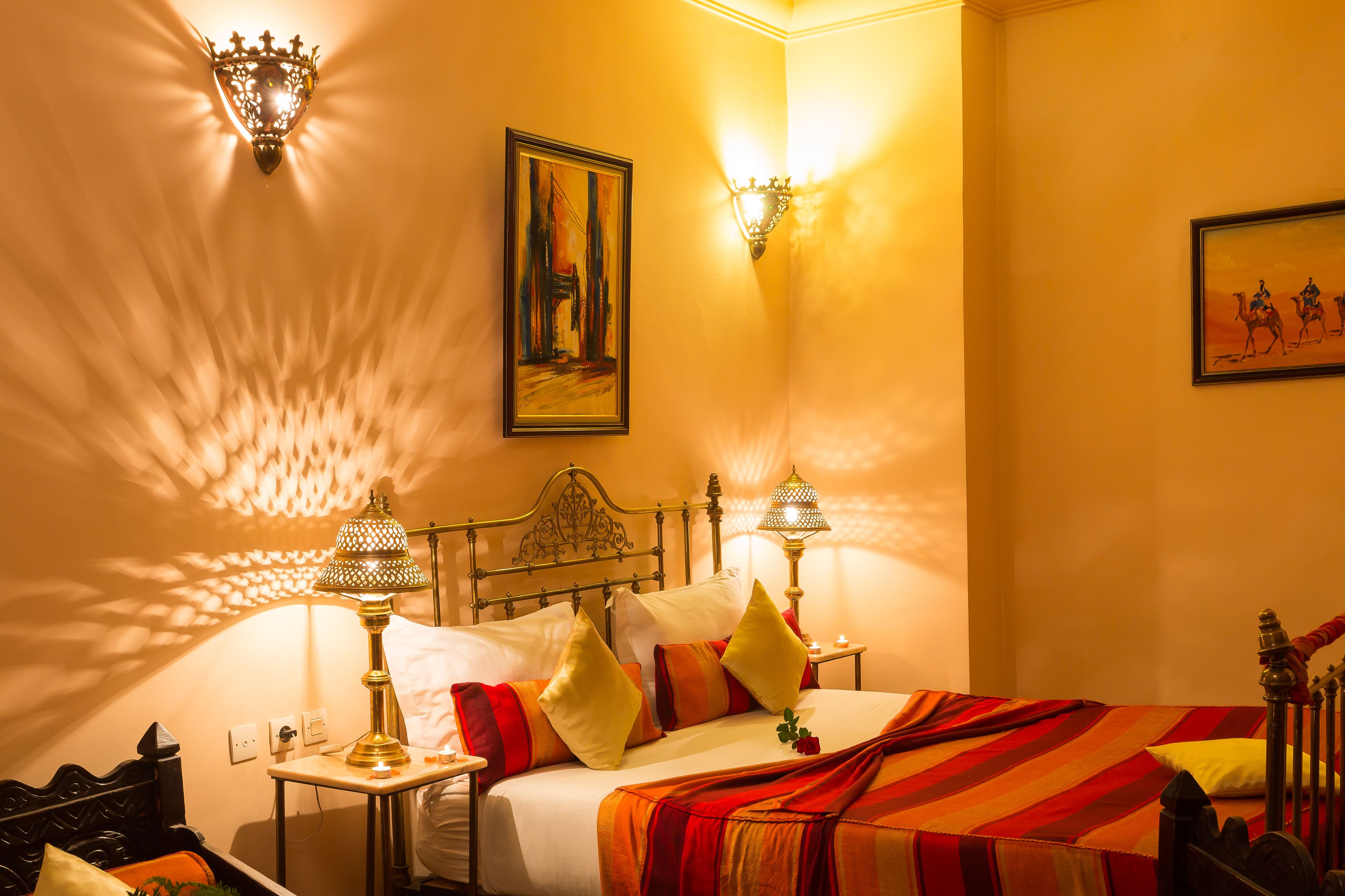 Una camera d'albergo con un letto, due applique, un quadro e una lampada.