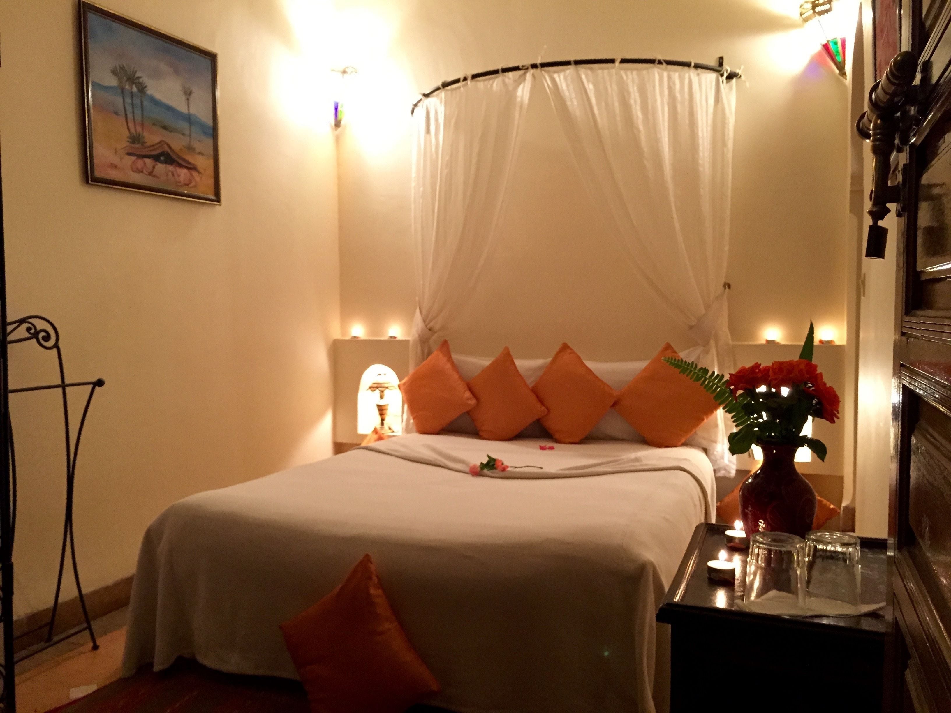A neatly arranged bedroom with a bed, a bedside table with a vase of flowers, and a wall-mounted lamp.