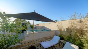 A rooftop pool area with a large umbrella, lounge chairs, and a small staircase leading to the pool.