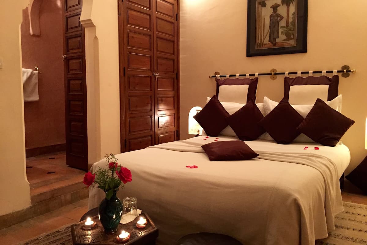 Una camera d'albergo con un letto, un armadio in legno, un quadro appeso al muro e un vaso con fiori sul comodino.