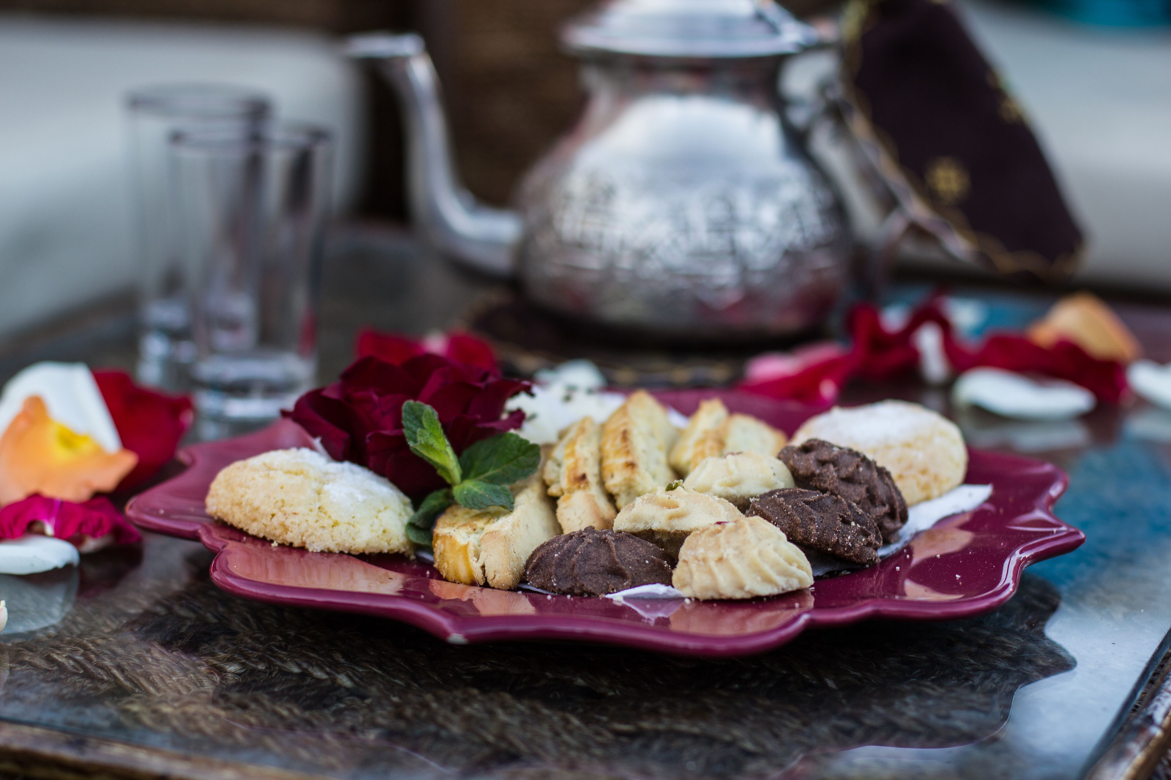 A table with a plate of assorted cookies and a teapot in the background.