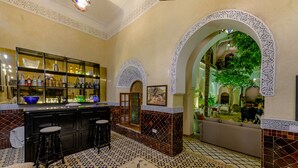 Zona bar con pavimento piastrellato, un bancone pieno di bottiglie e un’area salotto con divano e poltrone.