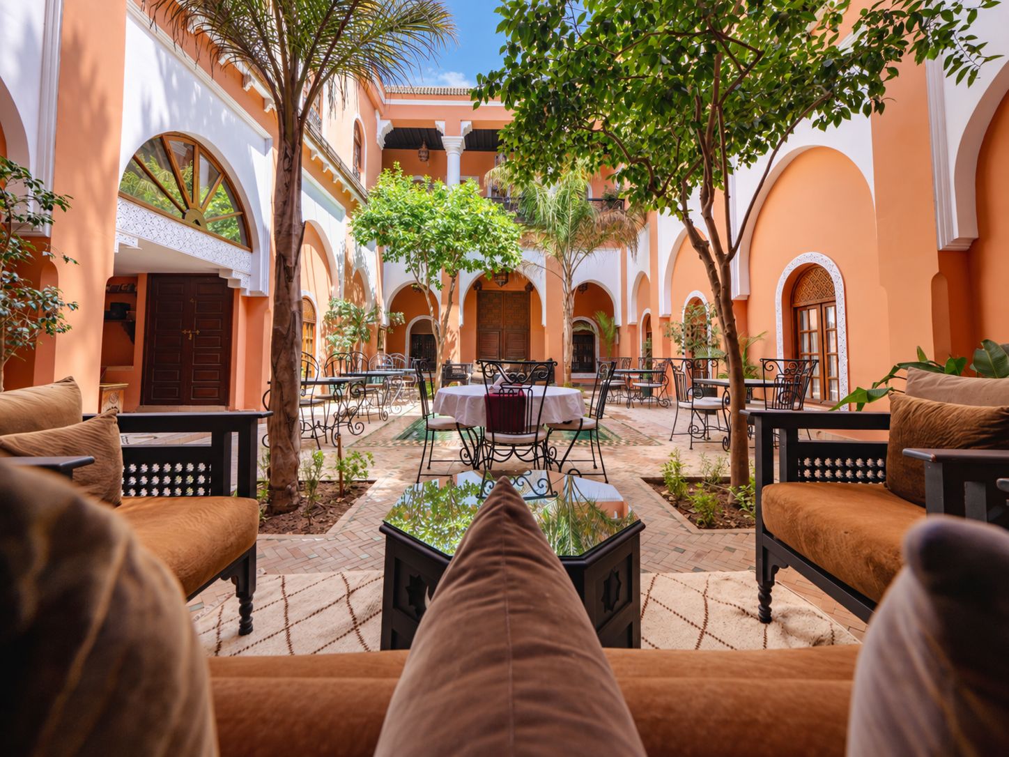 A courtyard with outdoor seating, palm trees, and a central table.