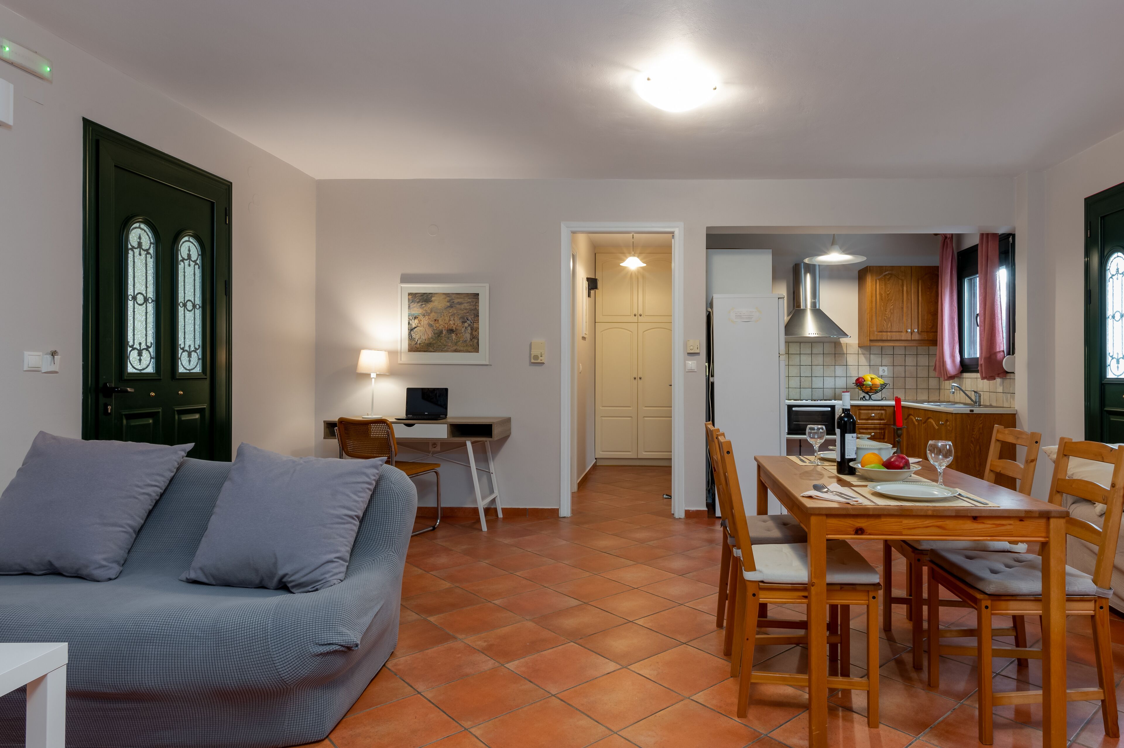Un salon avec un canapé, une table à manger avec des chaises, un coin cuisine avec des placards et un évier, et une porte avec des panneaux de verre.