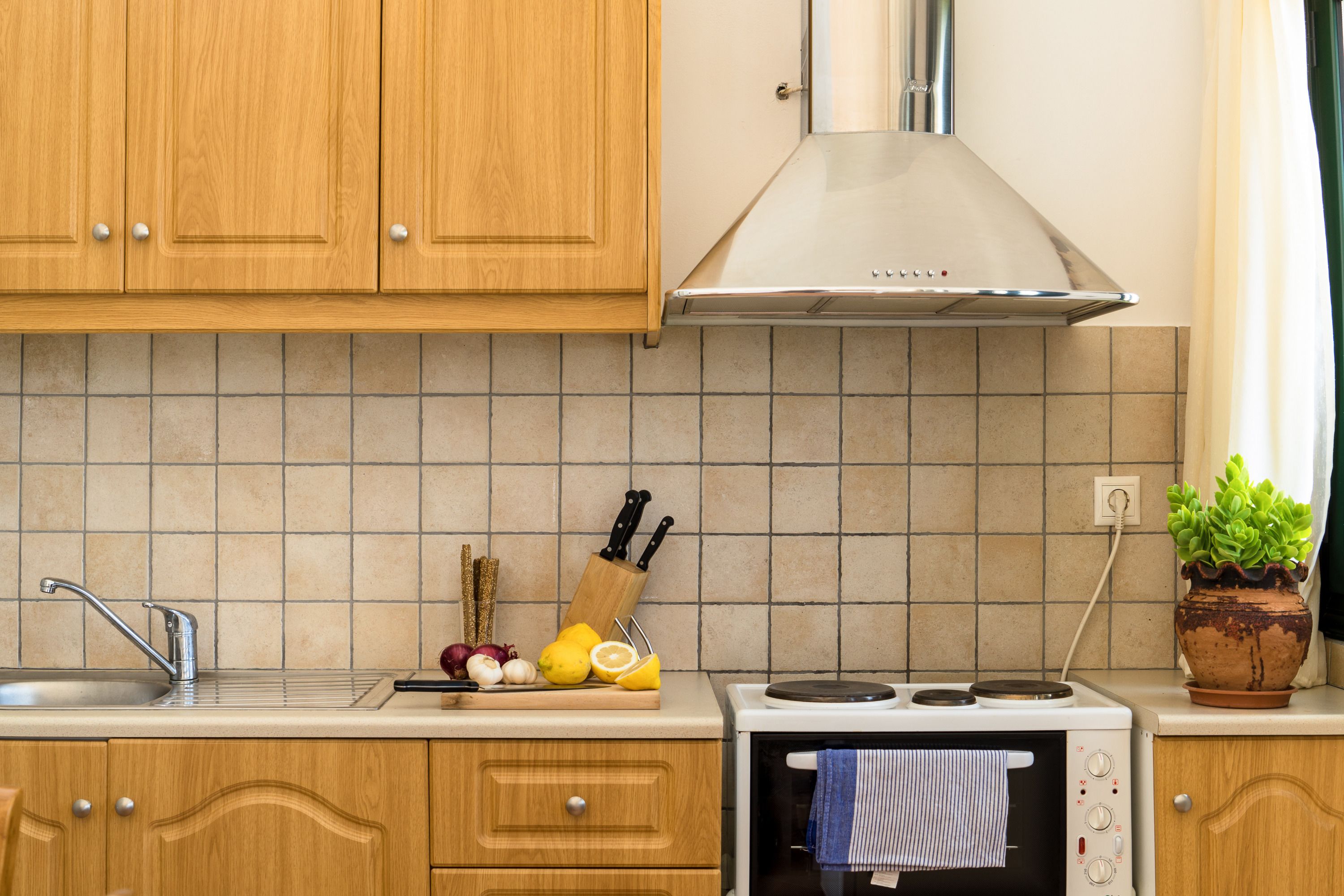Una cocina con gabinetes de madera, una campana extractora de acero inoxidable, un salpicadero de azulejos, un lavamanos y una estufa.