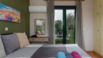 Ein Schlafzimmer mit Bett, Kissen, einem Nachttisch, einem Spiegel und Blick ins Freie.