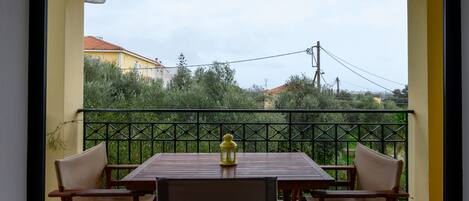 A balcony with a wooden table and two chairs, a yellow lantern, and a view of greenery and buildings.