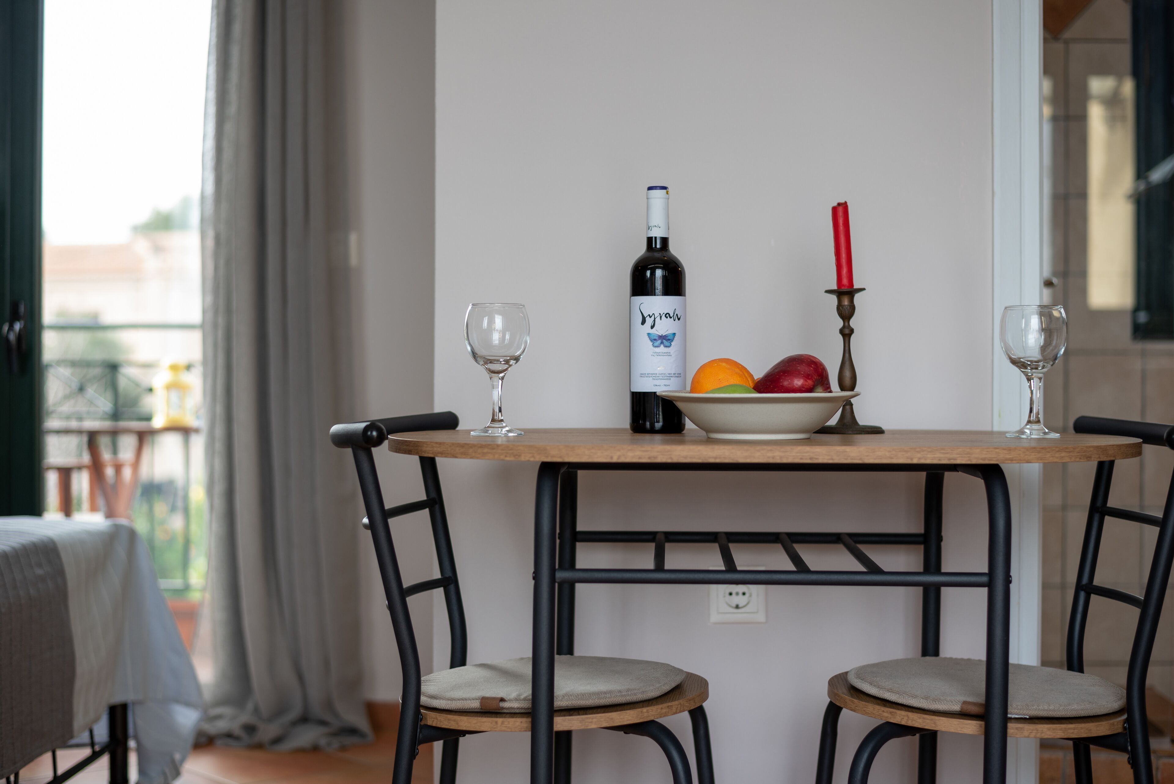 Una mesa de comedor con dos sillas, una botella de vino, un cuenco de fruta y una vela.