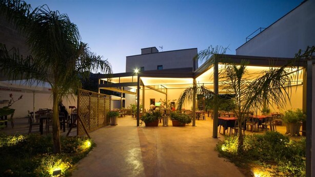 An outdoor patio area with tables and chairs, surrounded by plants and a fence.