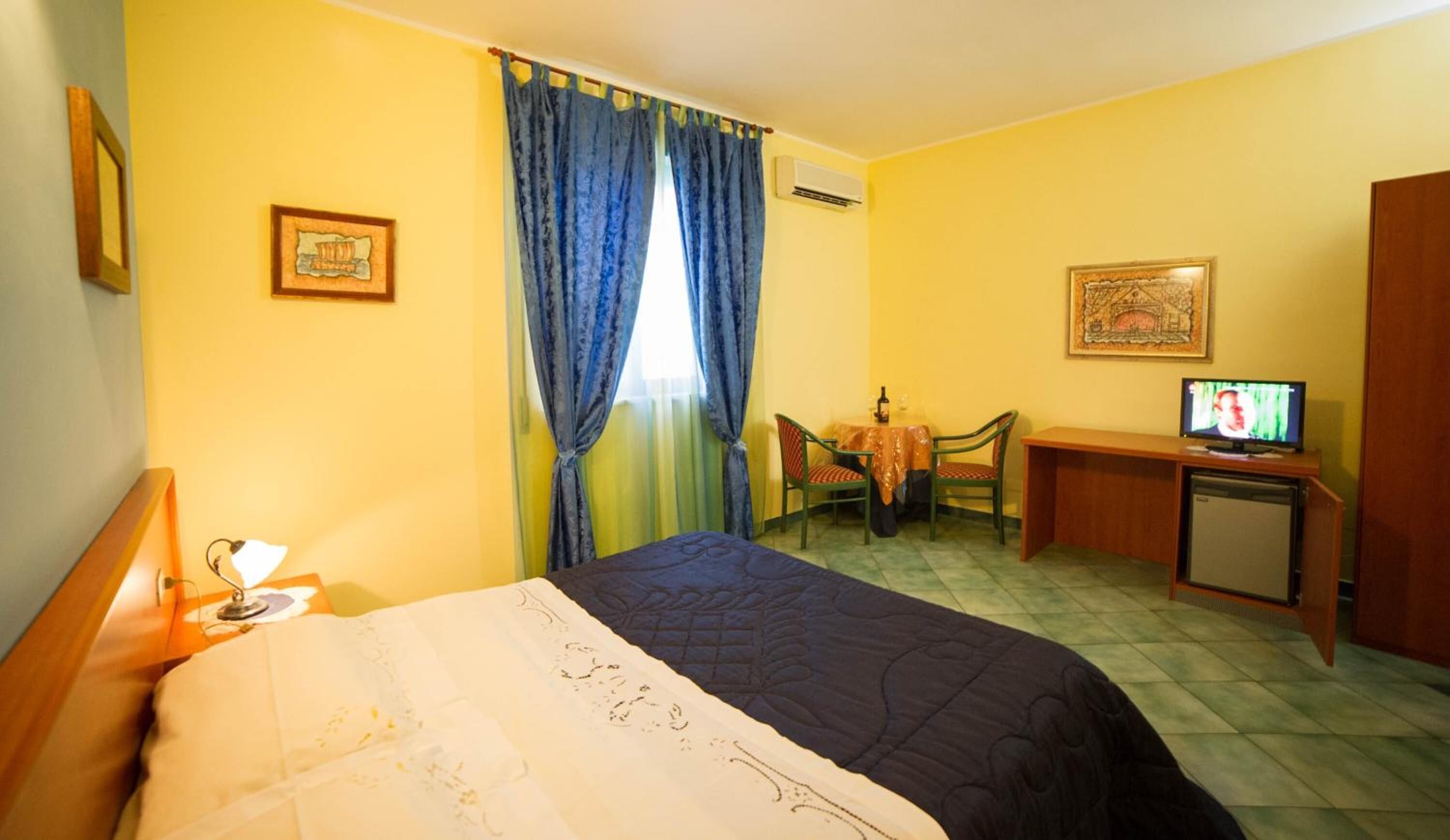 A hotel room with a bed, a desk, a chair, a television, and a small refrigerator.