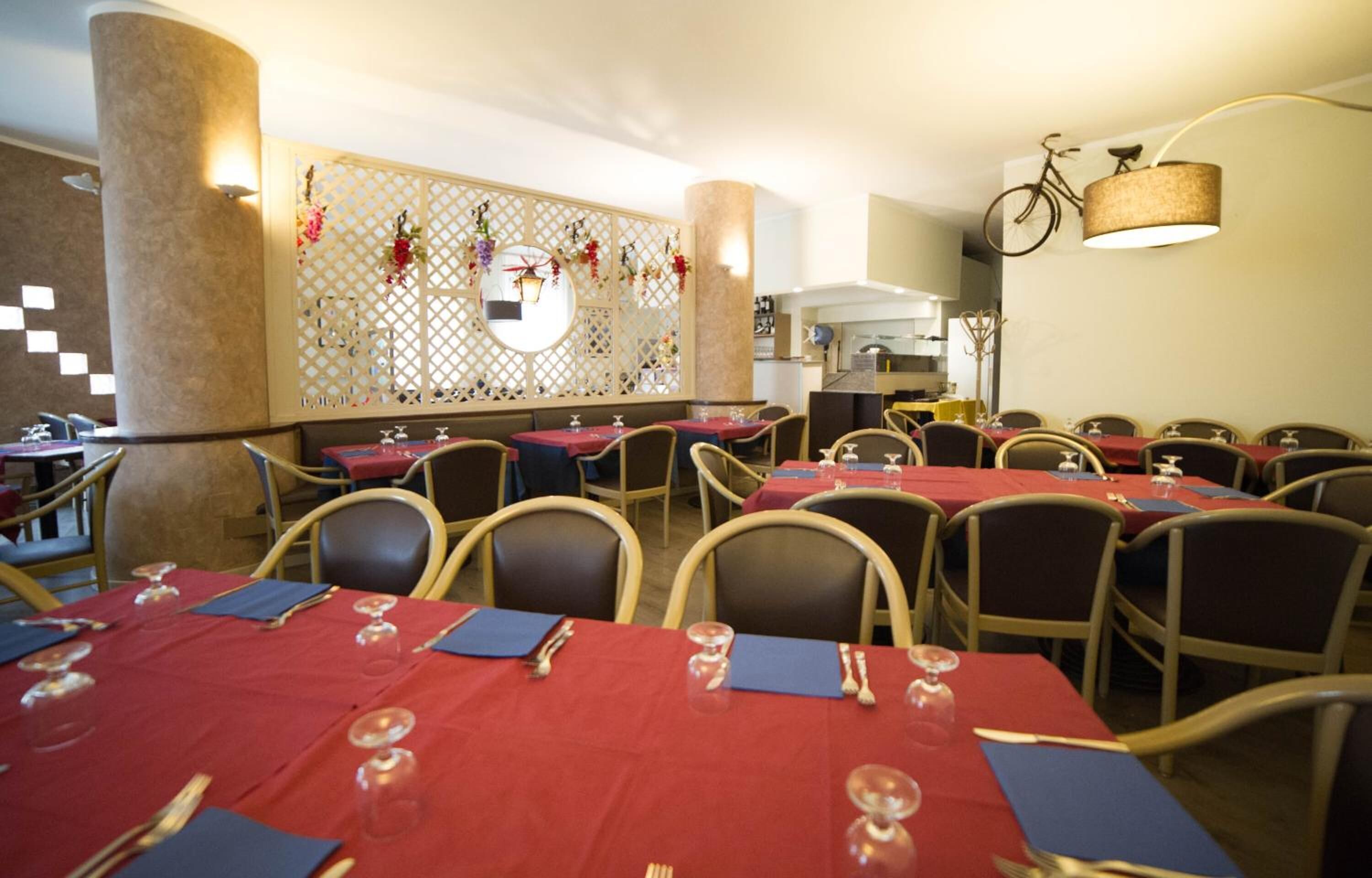 Un restaurant avec des tables rondes dressées pour le service, un mur décoratif orné de fleurs suspendues et un vélo accroché au mur.