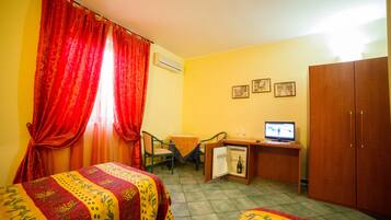 A room with two beds, a desk with a computer and a television, a small refrigerator, and a wardrobe.