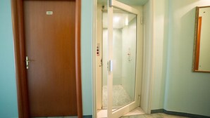 A hotel room with a wooden door marked '101', a glass elevator, and a mirror on the wall.