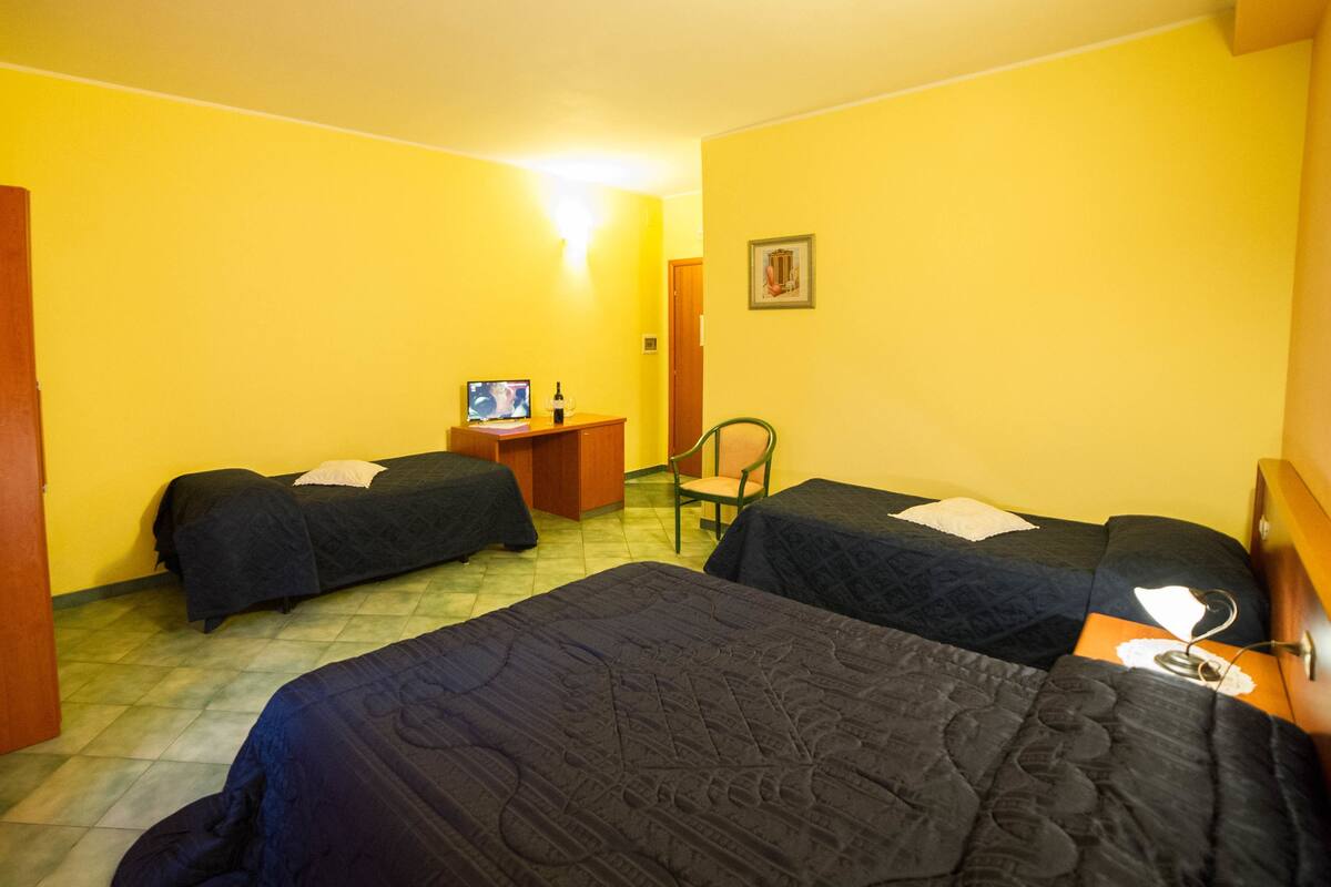 A hotel room with two single beds, a desk with a computer and a bottle, and a chair.