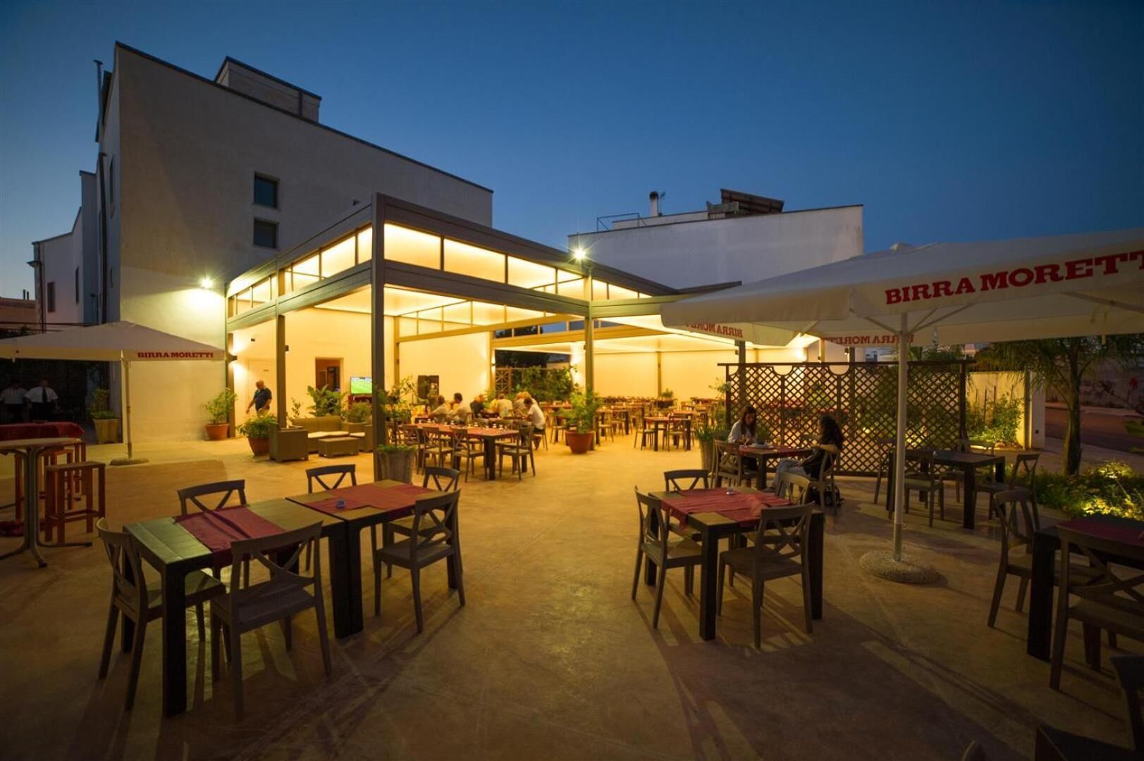 An outdoor dining area with tables and chairs, a covered seating area, and a building with signage.