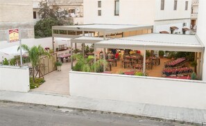 An outdoor dining area with multiple tables and chairs, surrounded by white walls and potted plants. - La Lanterna (Martano)