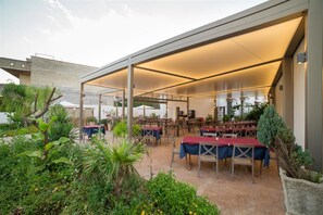 An outdoor dining area with tables and chairs, covered by a large canopy, surrounded by greenery and plants. - La Lanterna (Martano)