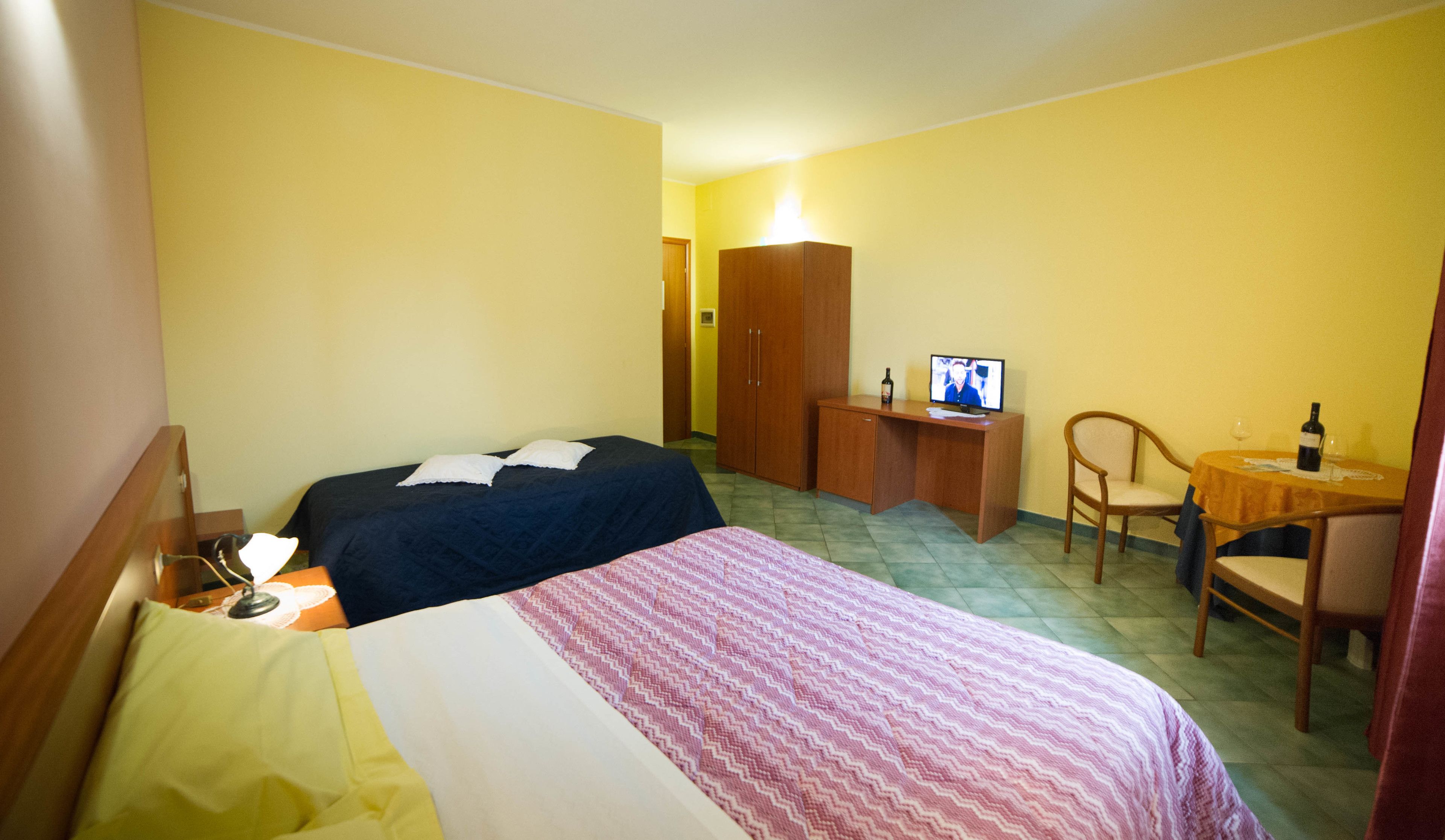 Una camera d'albergo con due letti, una scrivania con un computer, una sedia e un piccolo tavolo con una bottiglia e un bicchiere.
