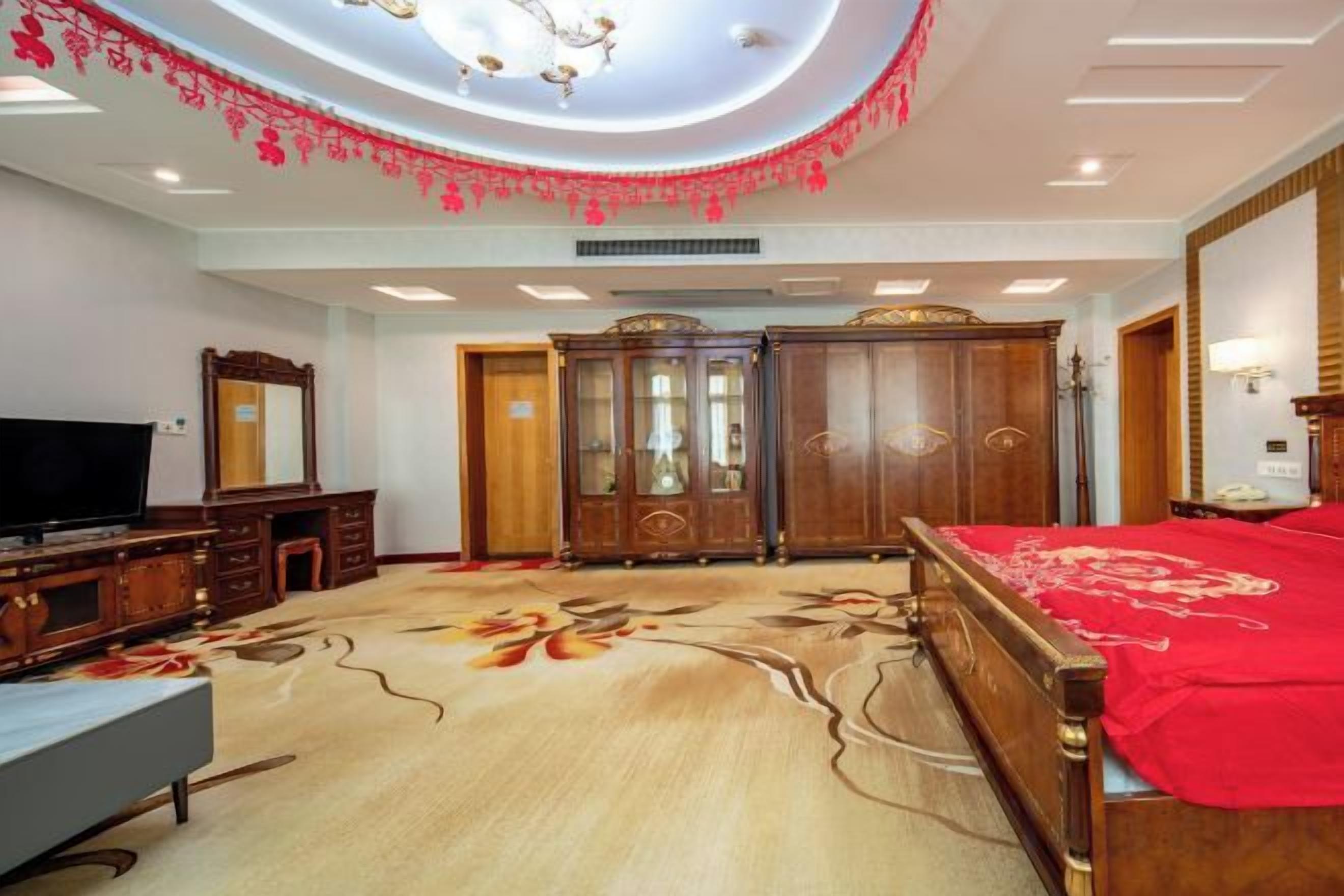 A hotel room with a large bed, a television, a wardrobe, and a carpeted floor.