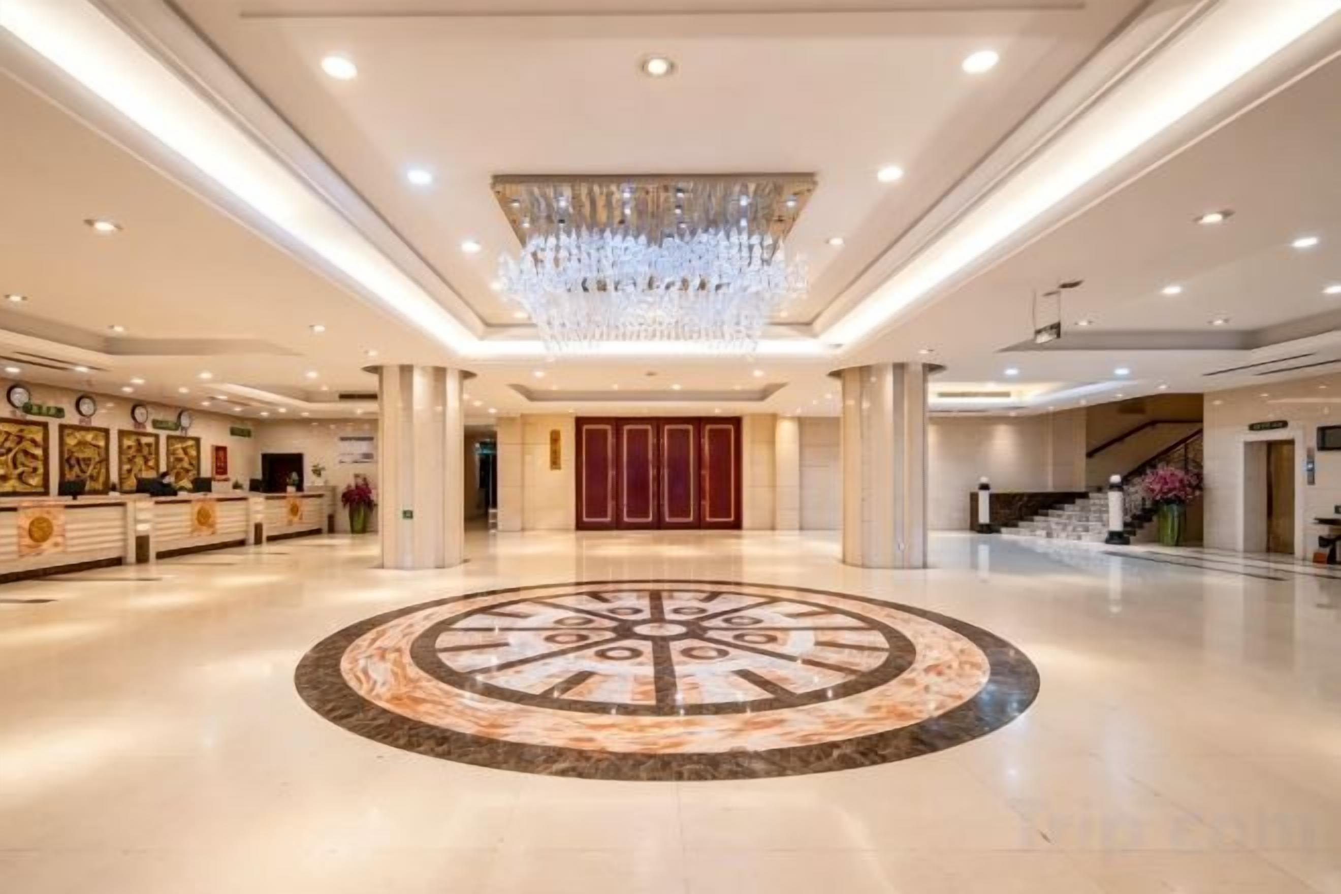A spacious lobby with a central circular floor design, a reception desk, and a staircase leading to upper floors.