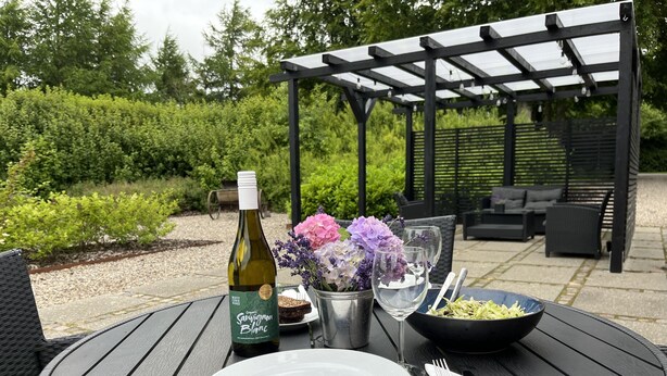 A round table set outdoors with a bottle of wine, a glass, a bowl of salad, and a plate. - Egebjerggaard Bed & Breakfast (Varde)
