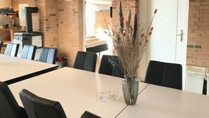 A conference room with a white table, black chairs, a vase with dried plants, and a brick wall. - Egebjerggaard Bed & Breakfast (Varde)