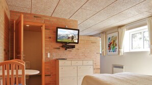 A room with a bed, a TV mounted on a brick wall, a wooden chair, a small table, and a window with curtains. - Egebjerggaard Bed & Breakfast (Varde)