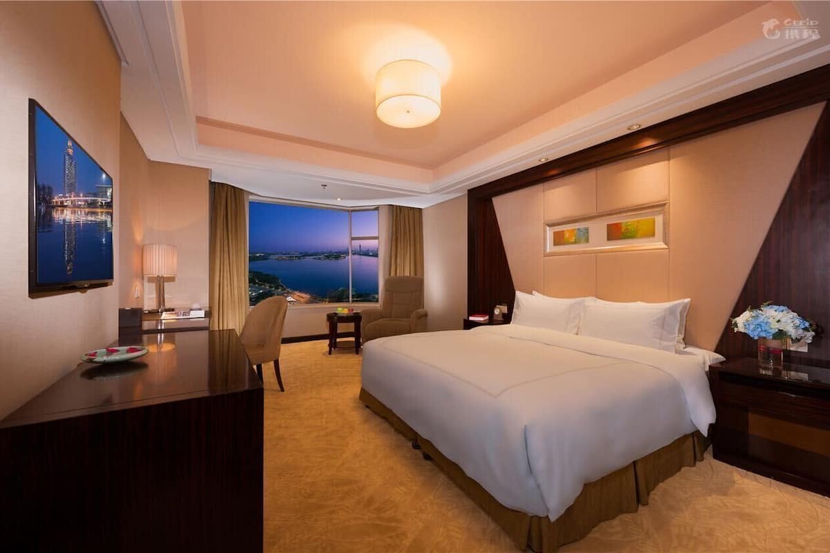 A hotel room with a large bed, a desk, a chair, and a view of a cityscape at night.