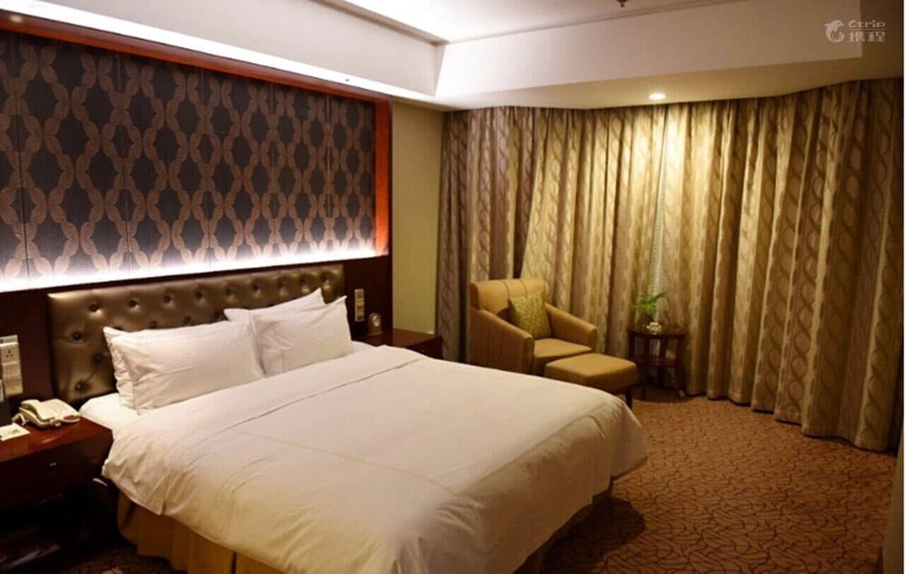 A hotel room with a large bed, a chair, a nightstand, and a curtain.