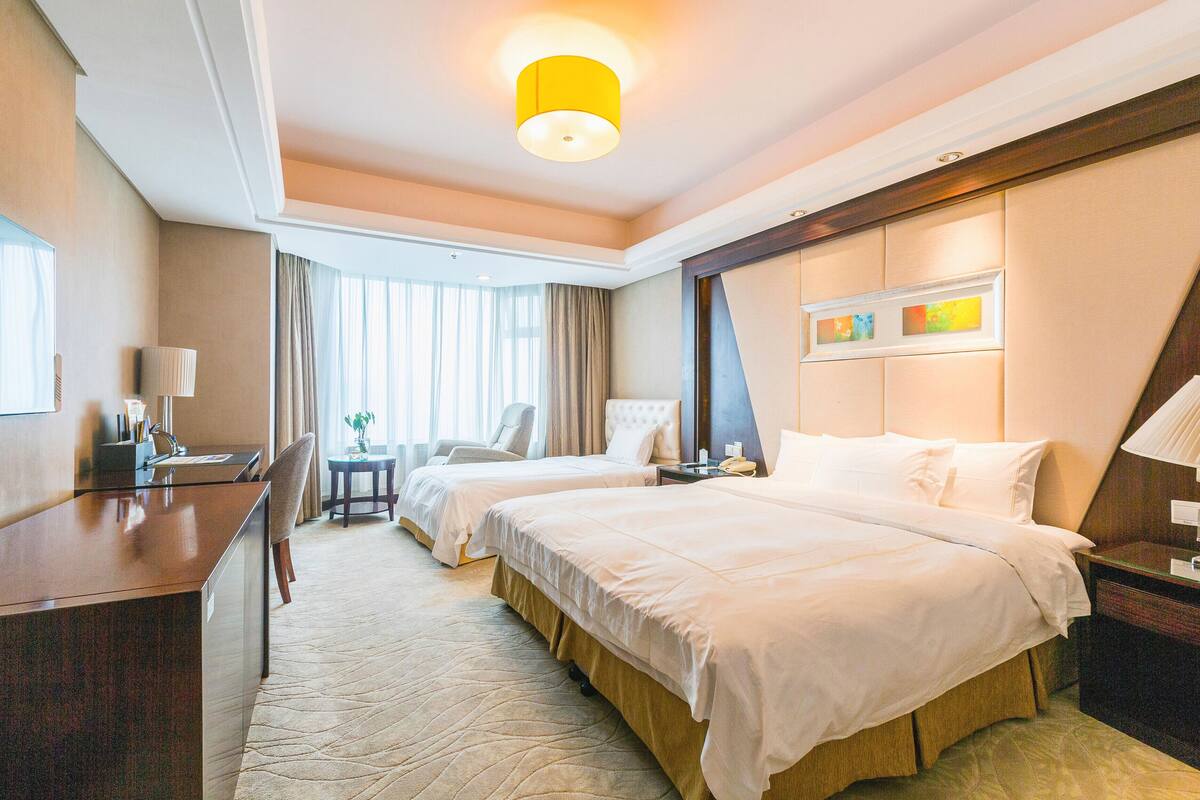 A hotel room with two beds, a desk, a chair, a small table, and a window with curtains.