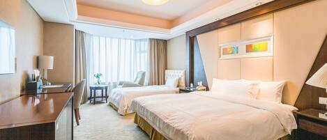 A hotel room with two beds, a desk, a chair, a small table, and a window with curtains.