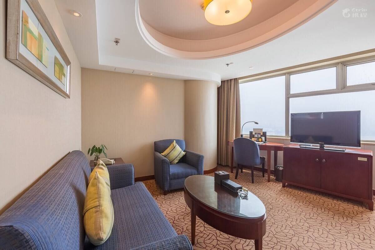 A hotel room with a sofa, armchair, coffee table, TV, and a desk with a chair.