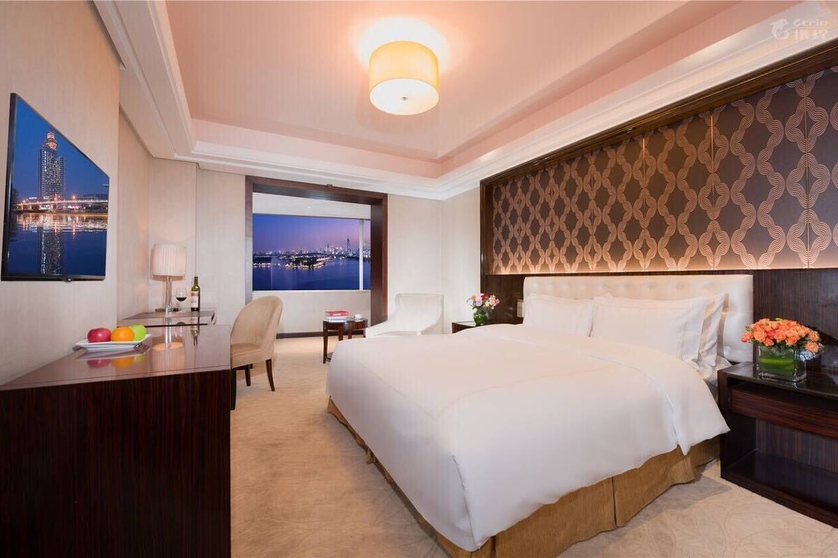 A hotel room with a large bed, a desk with a chair, a TV, and a view of a cityscape.