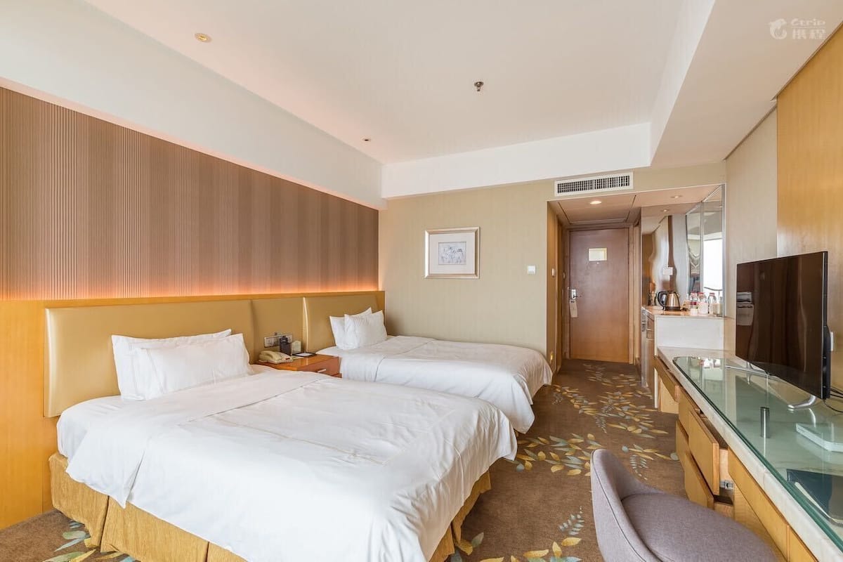A hotel room with two beds, a TV, a desk, and a bathroom visible through an open door.