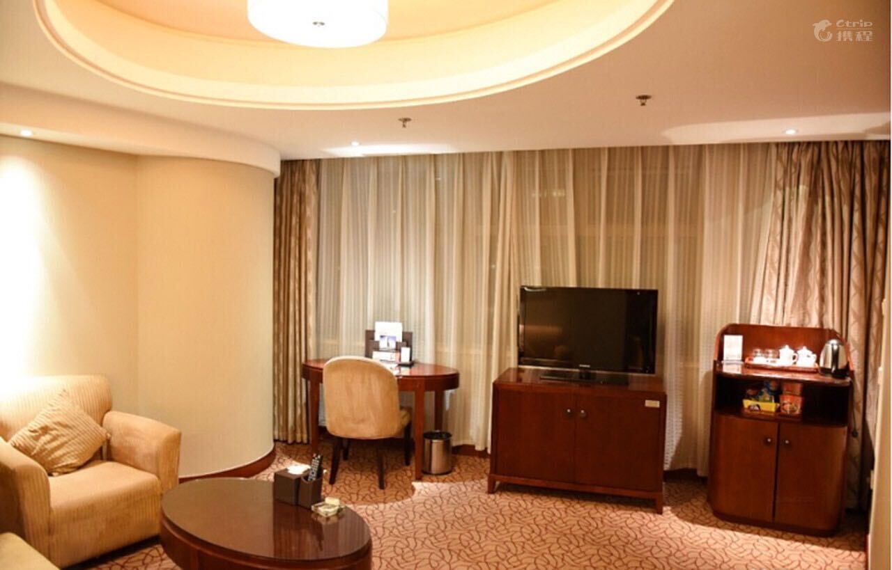 A hotel room with a sofa, a coffee table, a TV, a small desk with a chair, and a cabinet.