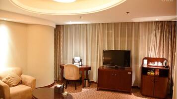 Quarto de hotel com sofá, mesa de centro, televisão, pequena escrivaninha com cadeira e armário.