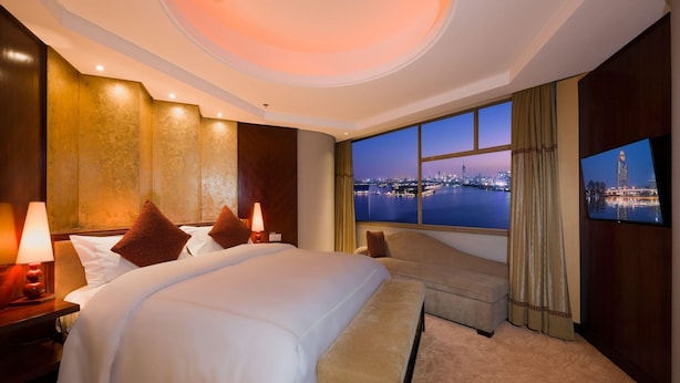 A hotel room with a large bed, a bench, a TV, and a view of a cityscape at night. - Shuguang International Hotel Nanjing (Nanjing)