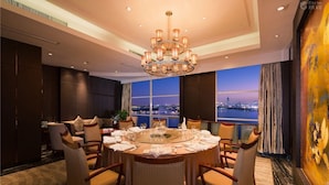 A dining room with a round table set for six, surrounded by chairs, with a cityscape view through large windows. - Shuguang International Hotel Nanjing (Nanjing)