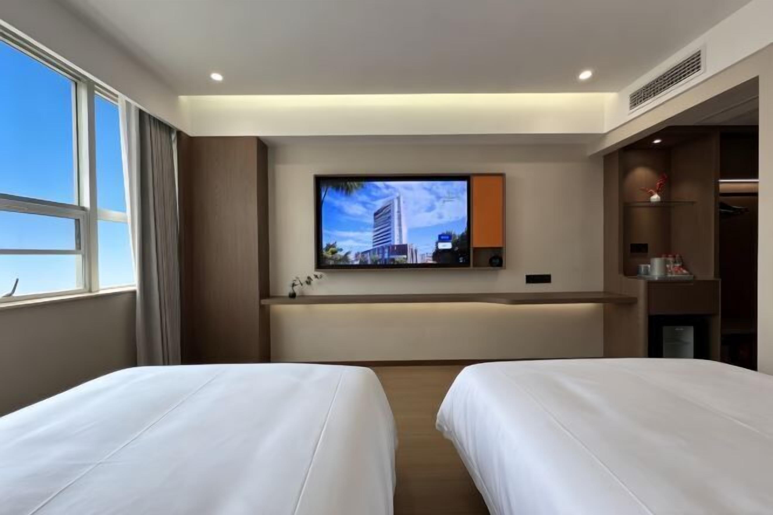 Une chambre d’hôtel avec deux lits, un téléviseur fixé au mur, une fenêtre et un petit bureau.