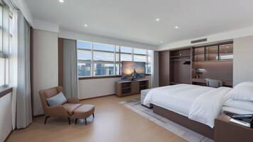 A modern hotel room with a large bed, a desk, a chair, and a view of the city.