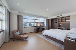Habitación de hotel moderna con una cama grande, un escritorio, una silla y vistas a la ciudad.