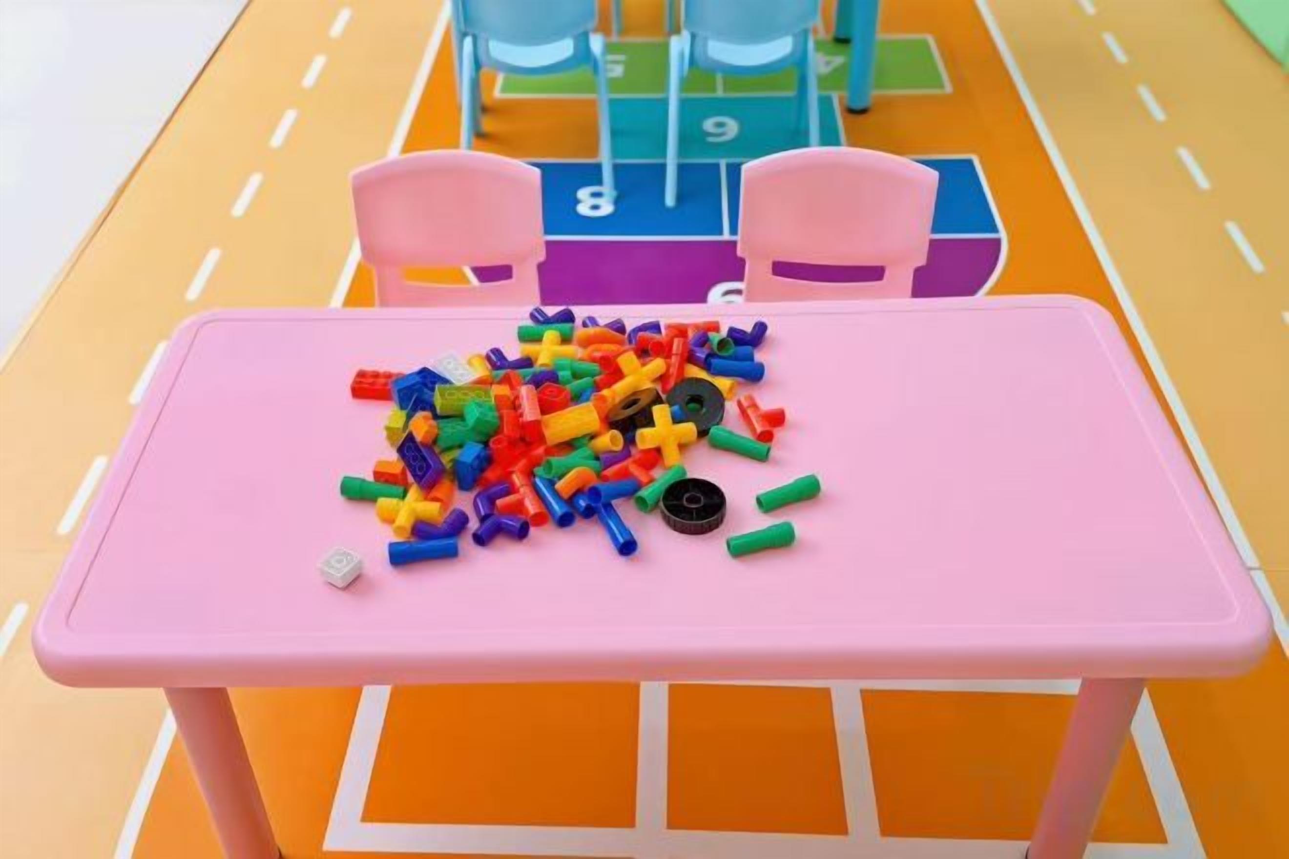 A pink table with colorful building blocks on it, set on a colorful play mat with numbers and chairs.