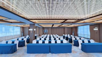 Un salón de conferencias con filas de mesas y sillas, ventanas amplias y un diseño moderno en el techo.