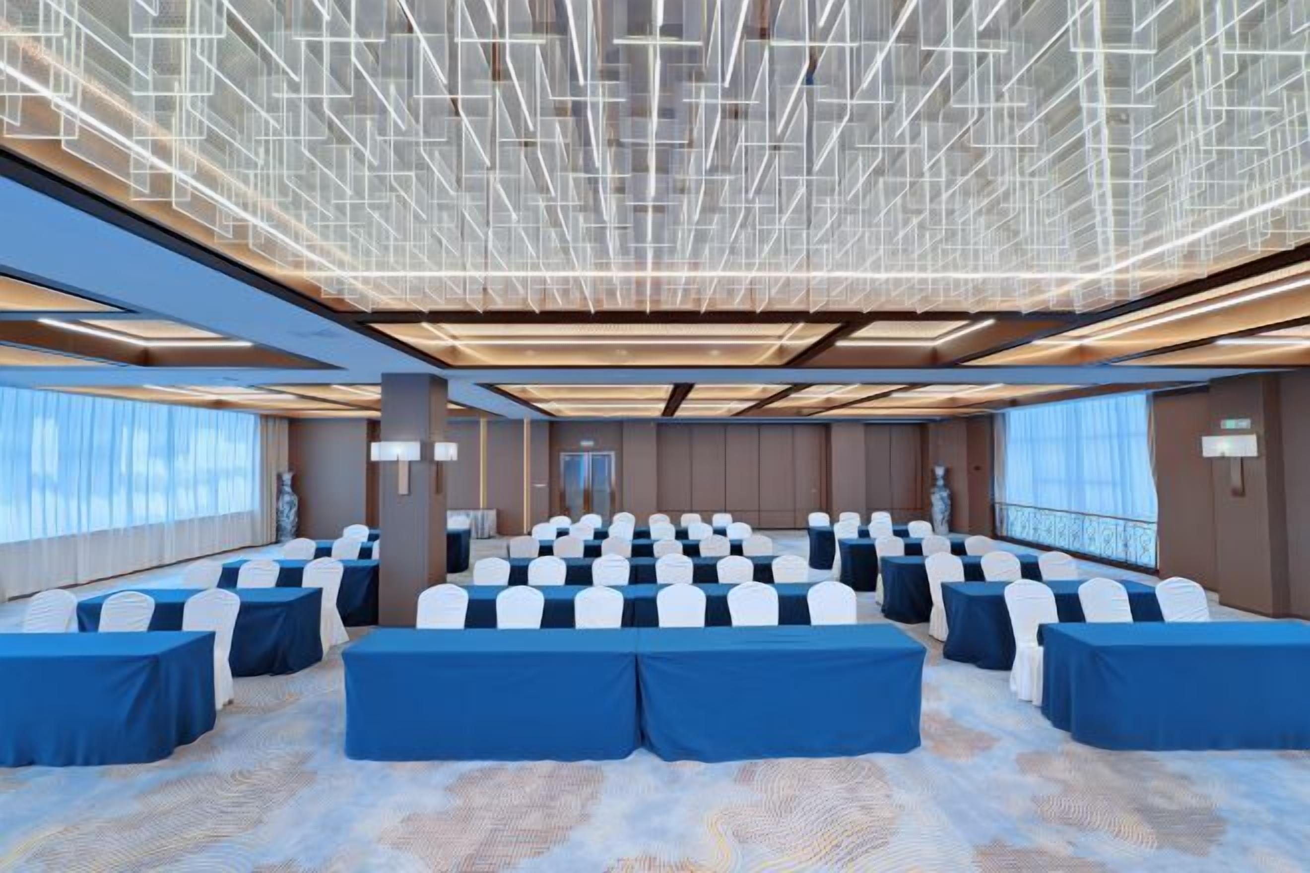 A conference room with rows of tables and chairs, large windows, and a modern ceiling design. - Artwell International Hotel (RIZHAO)